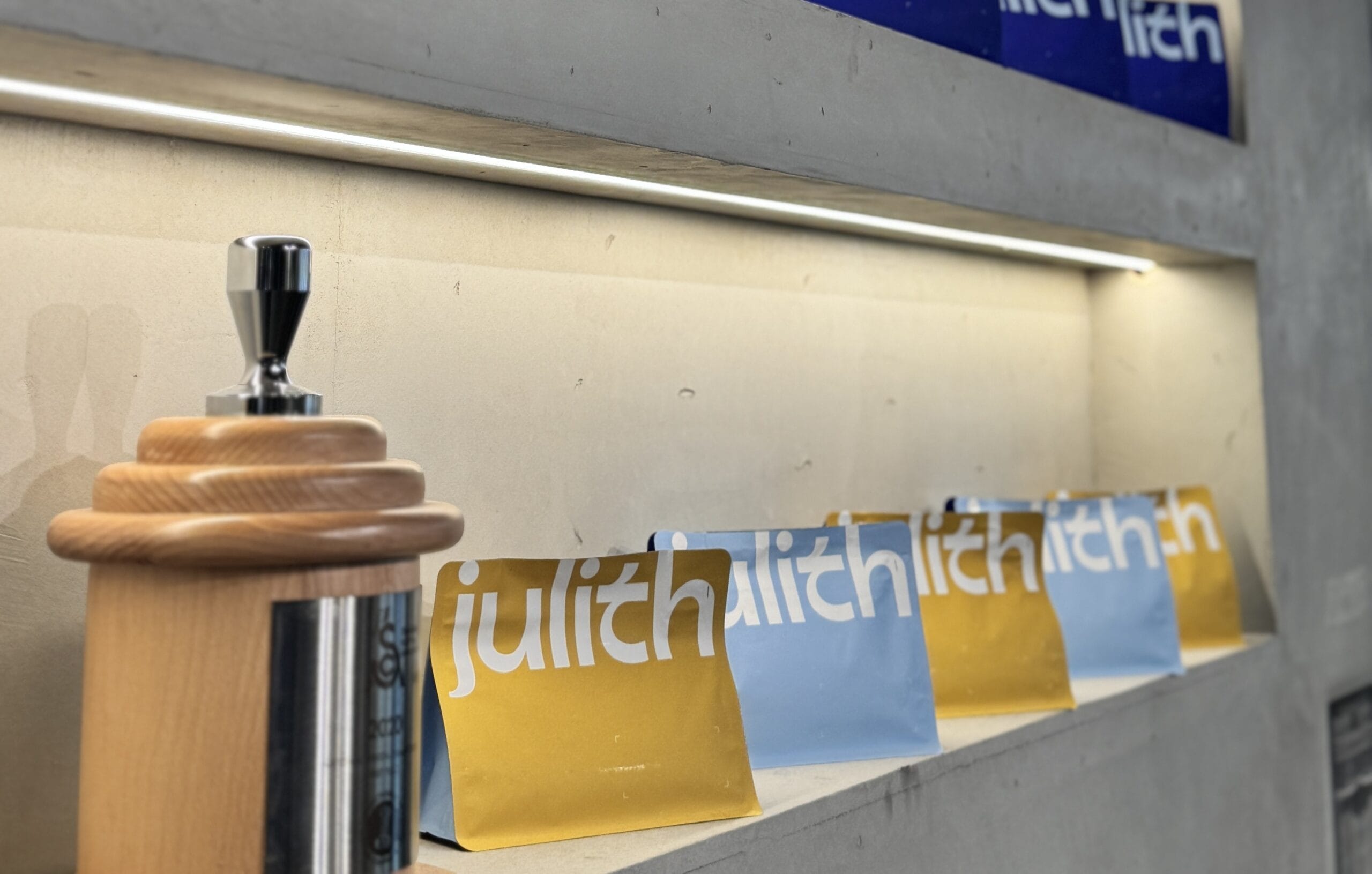 Shelf display with Julith Coffee yellow and blue coffee bags next to a wooden espresso tamper