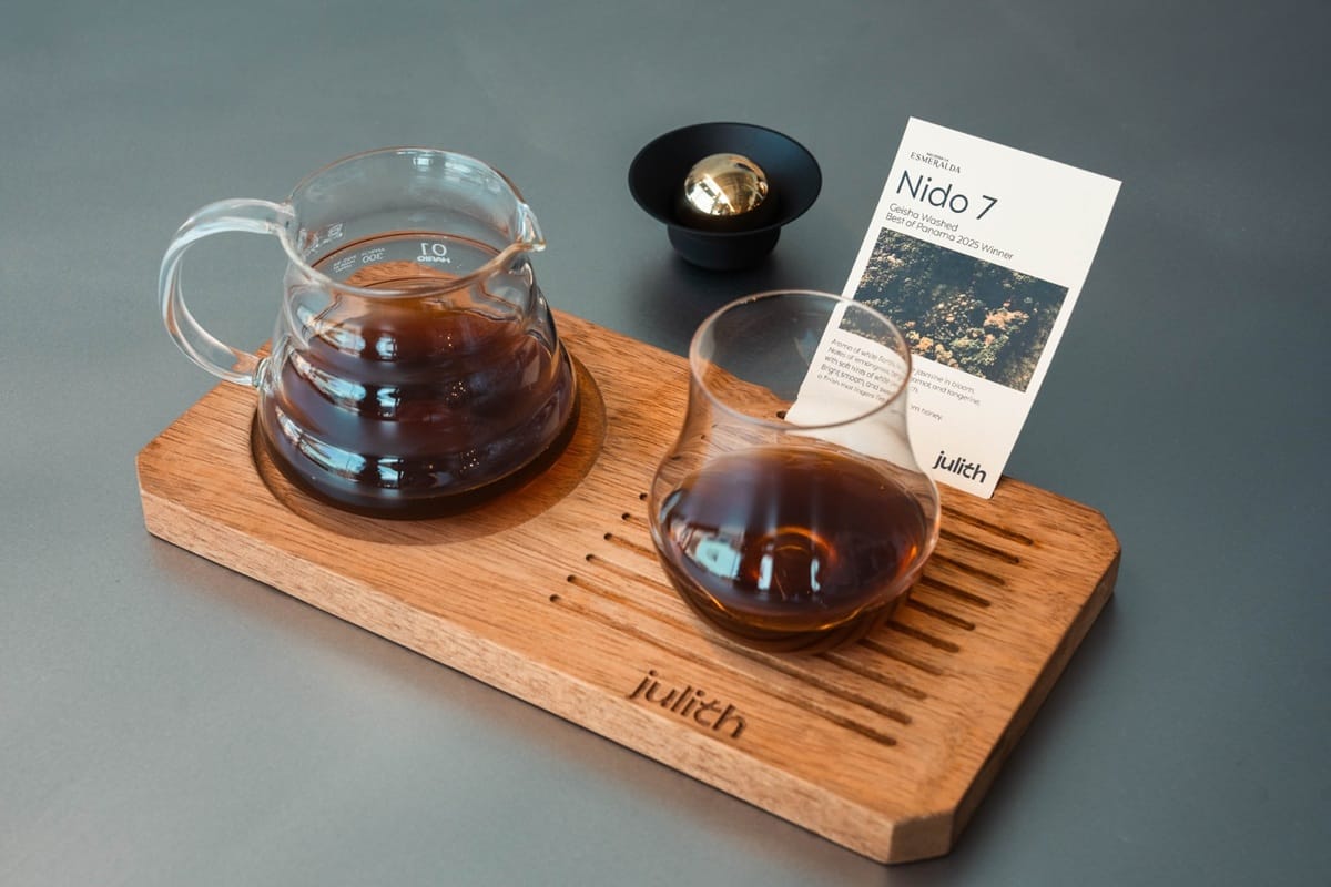 Wooden serving board with a glass coffee carafe and a hot black coffee in a small glass cup